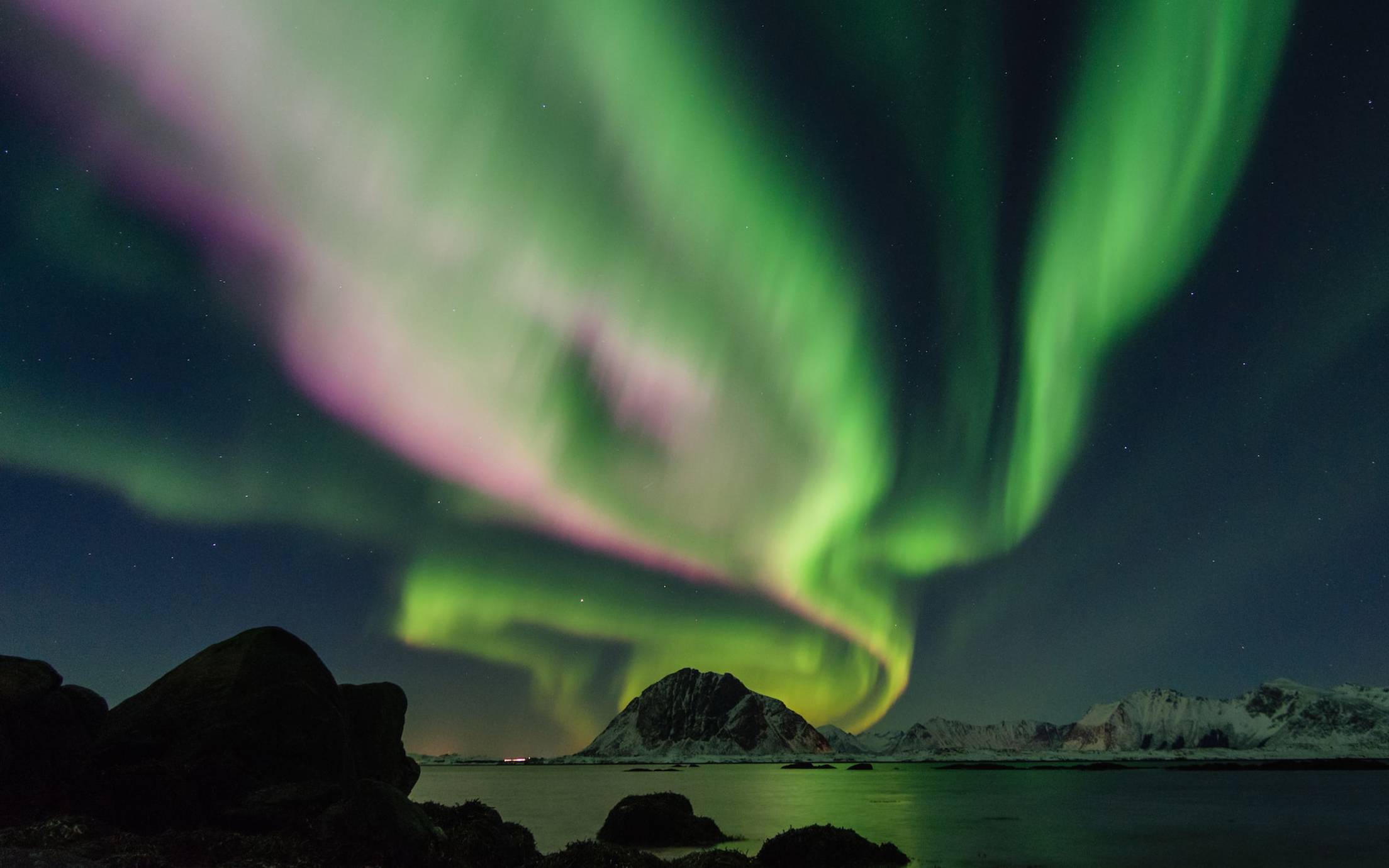 Northern lights over a lake and snow covered mountains